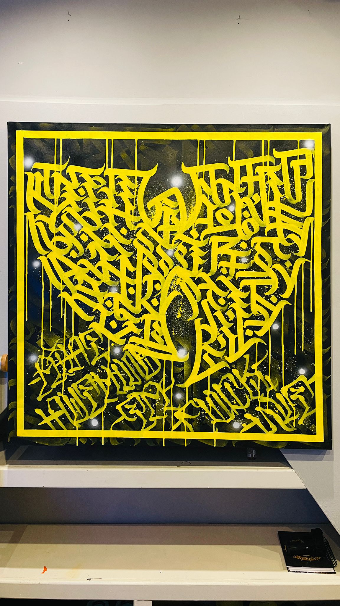Full view of Burnzy’s Wu artwork – yellow calligraphy on black background, acrylic on 40x40 canvas, mounted on wall.