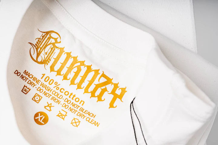 Close-up view of the Burnzy Art woven logo tag sewn onto the white t-shirt, emphasizing branding details.
